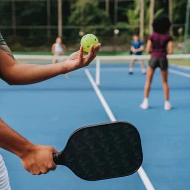Player holding a pickleball paddle and ball on a blue court