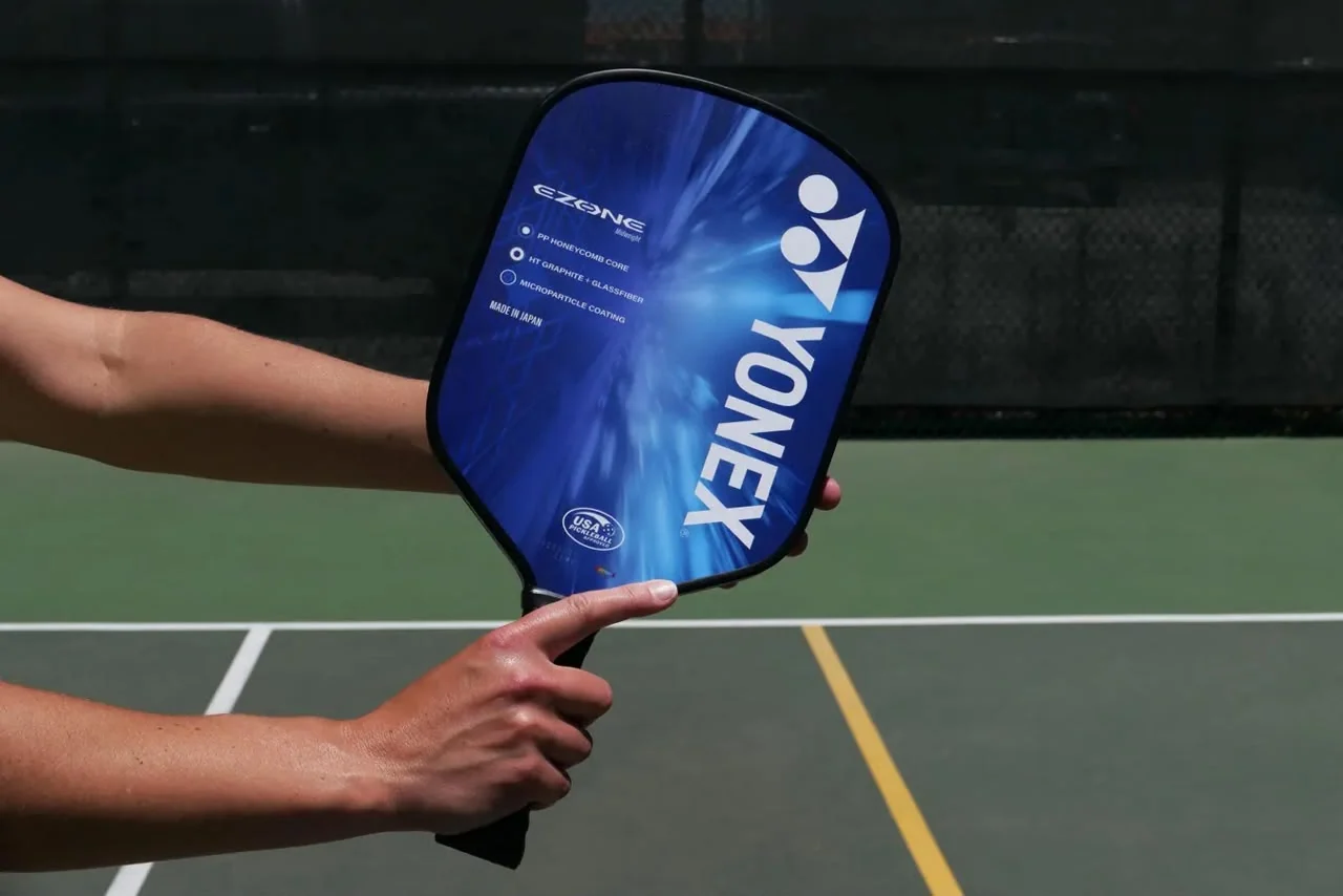 Player holding a graphite pickleball paddle on an outdoor court